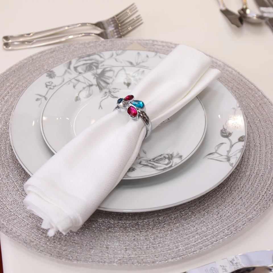 A silver table setting with a colourful jewelled napkin ring